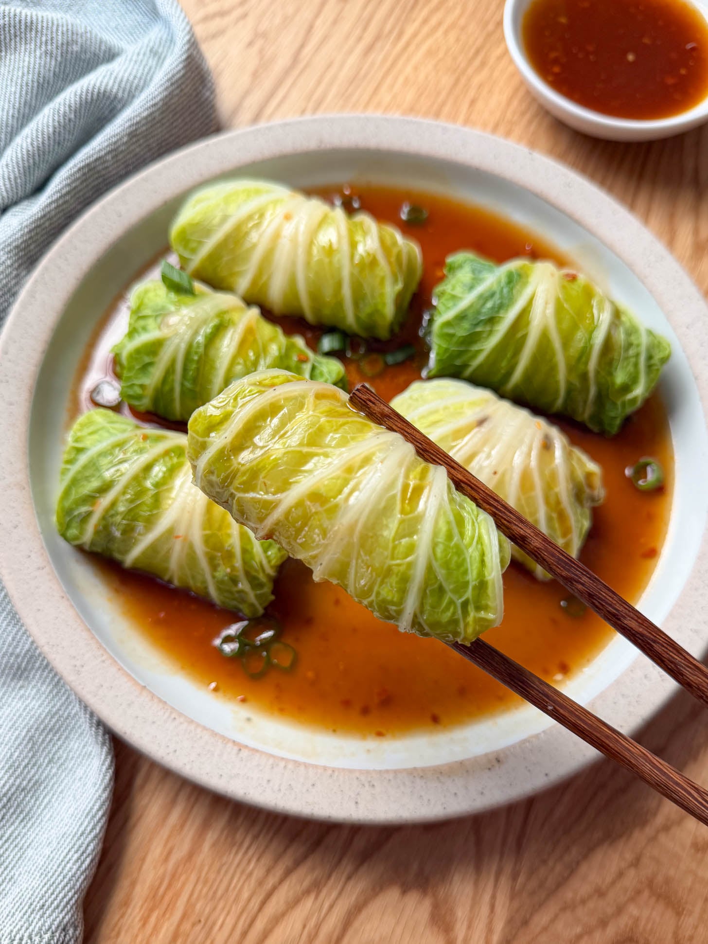 Chinese stuffed napa cabbage roll held with chopsticks over a plate of steamed cabbage rolls
